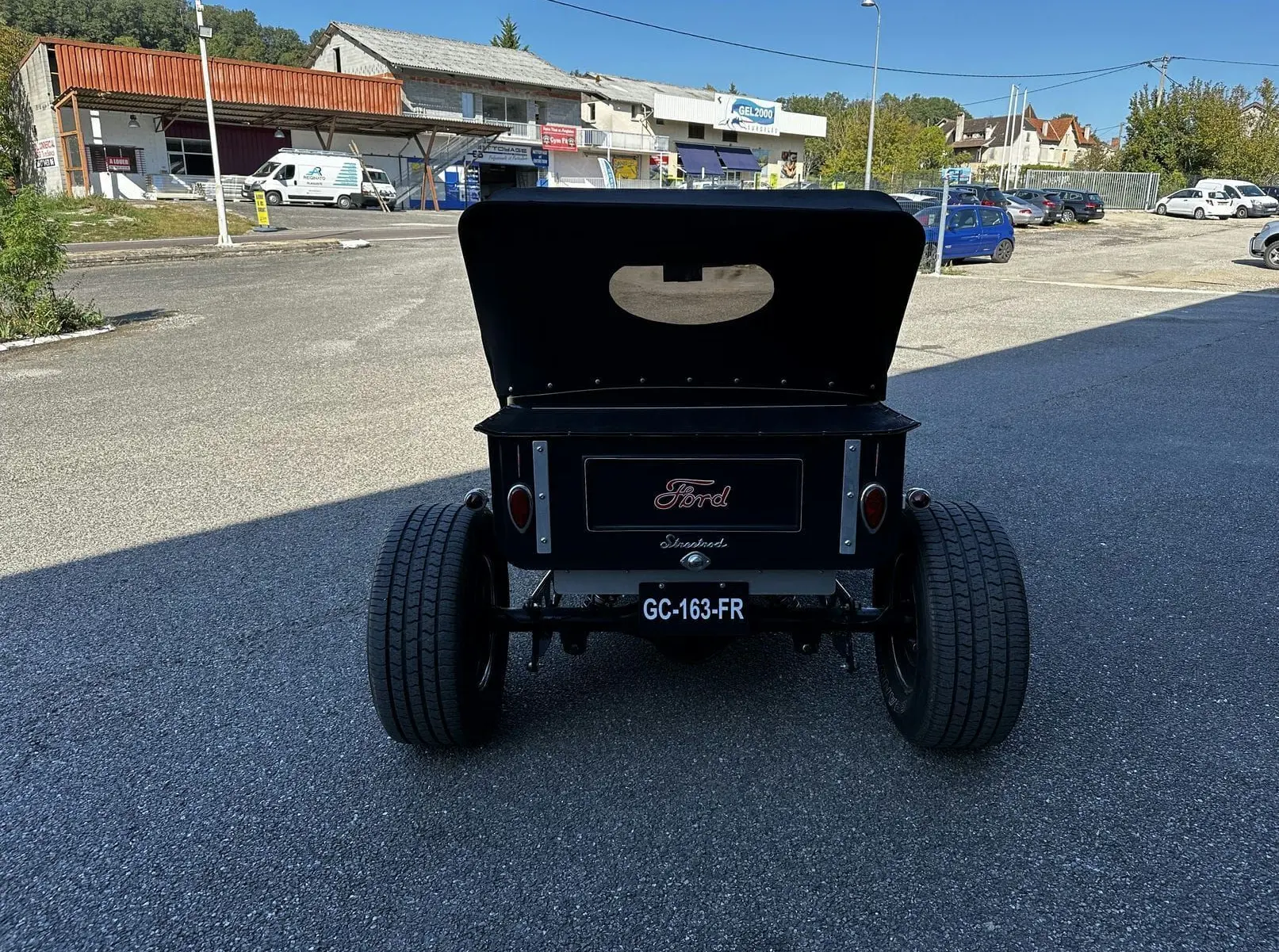 Vue arrière d'une Ford T Hot Rod V8 noire de 1923 avec capote relevée et larges pneus arrière visibles.