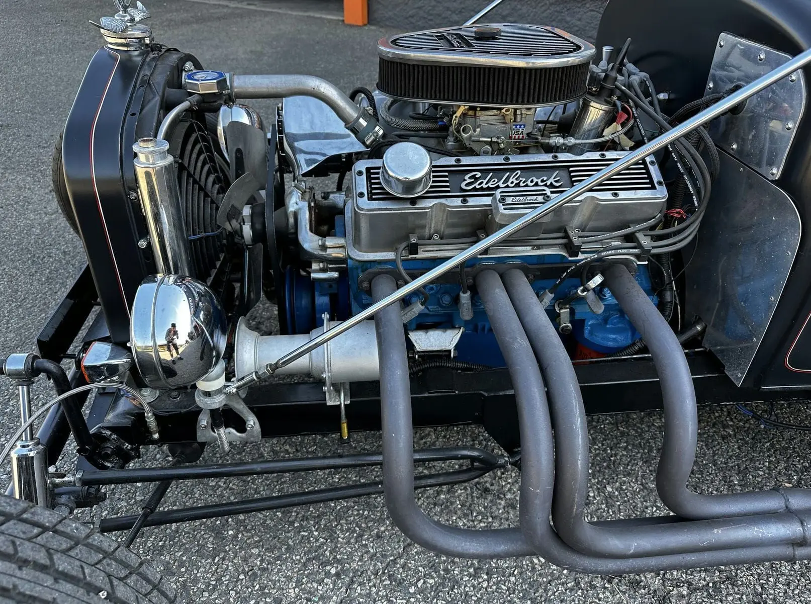 Gros plan sur le moteur V8 Edelbrock bleu et gris du Ford T Hot Rod noir, avec échappements latéraux visibles.