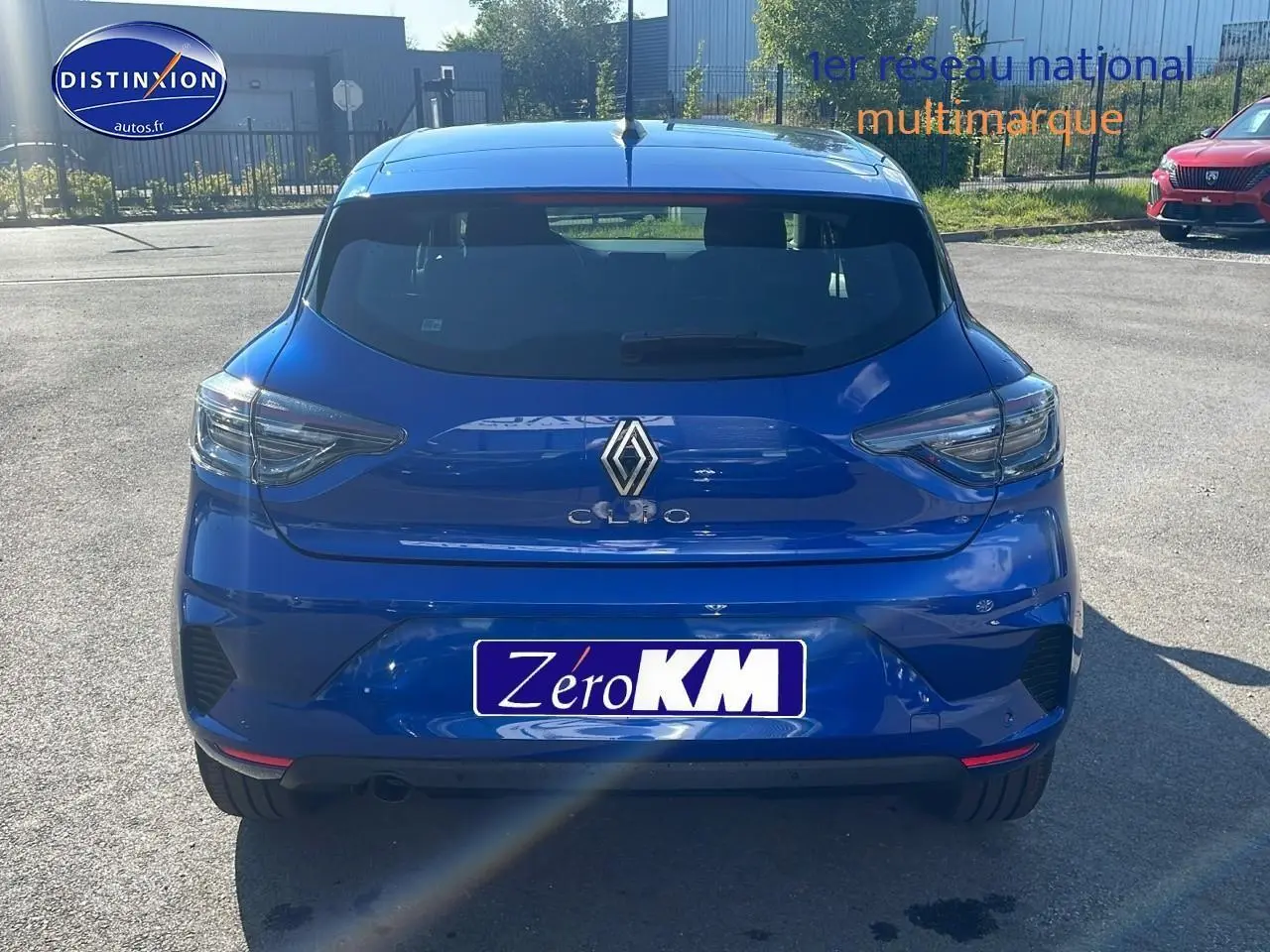 Vue arrière d'une Renault Clio V bleu iron garée en extérieur avec feux arrière LED et becquet distinctif.