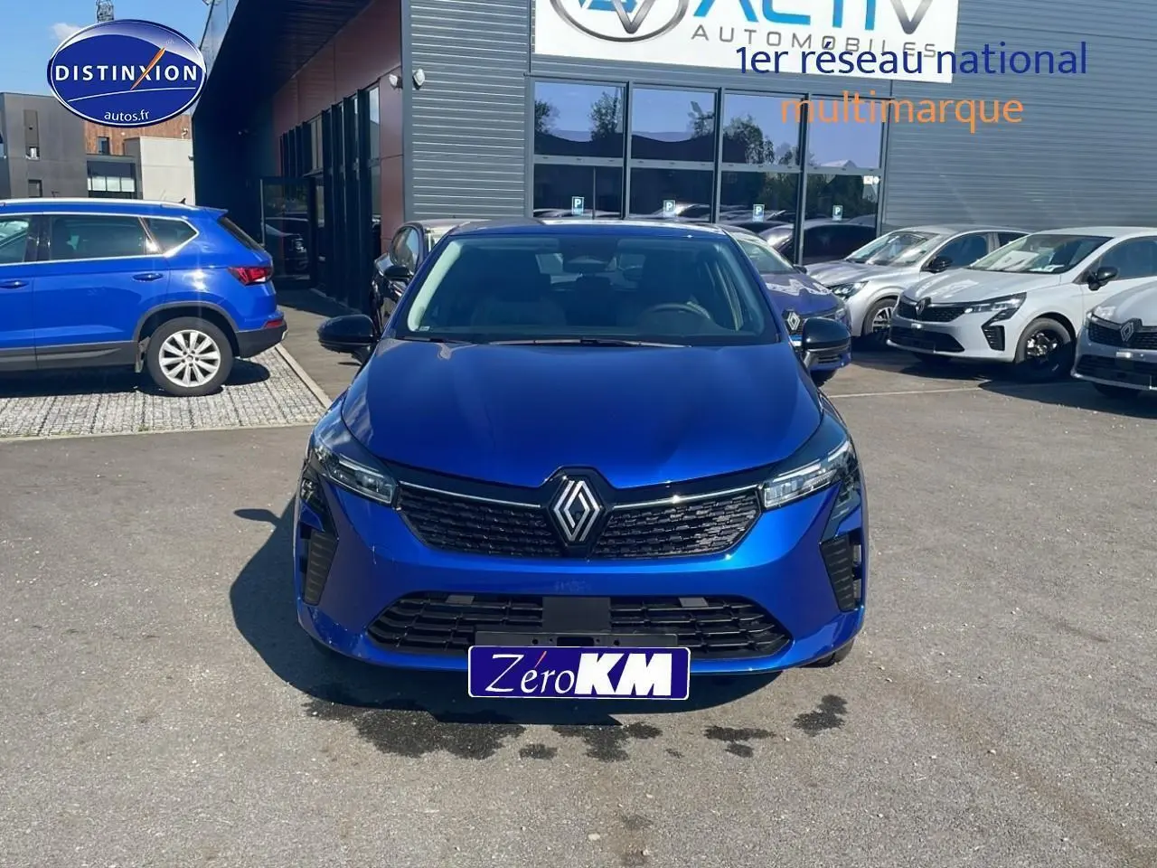 Vue frontale d'une Renault Clio V bleu iron avec calandre noire et logo Renault proéminent, stationnée en extérieur.