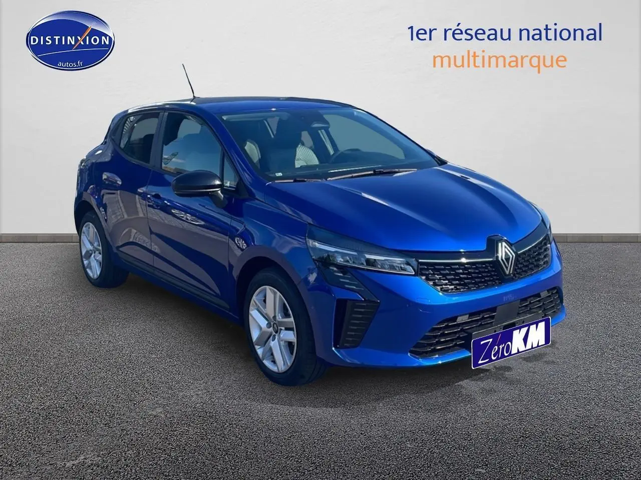 Renault Clio V bleu iron vue 3/4 avant droit, avec calandre noire et jantes argentées sur sol bitumé.