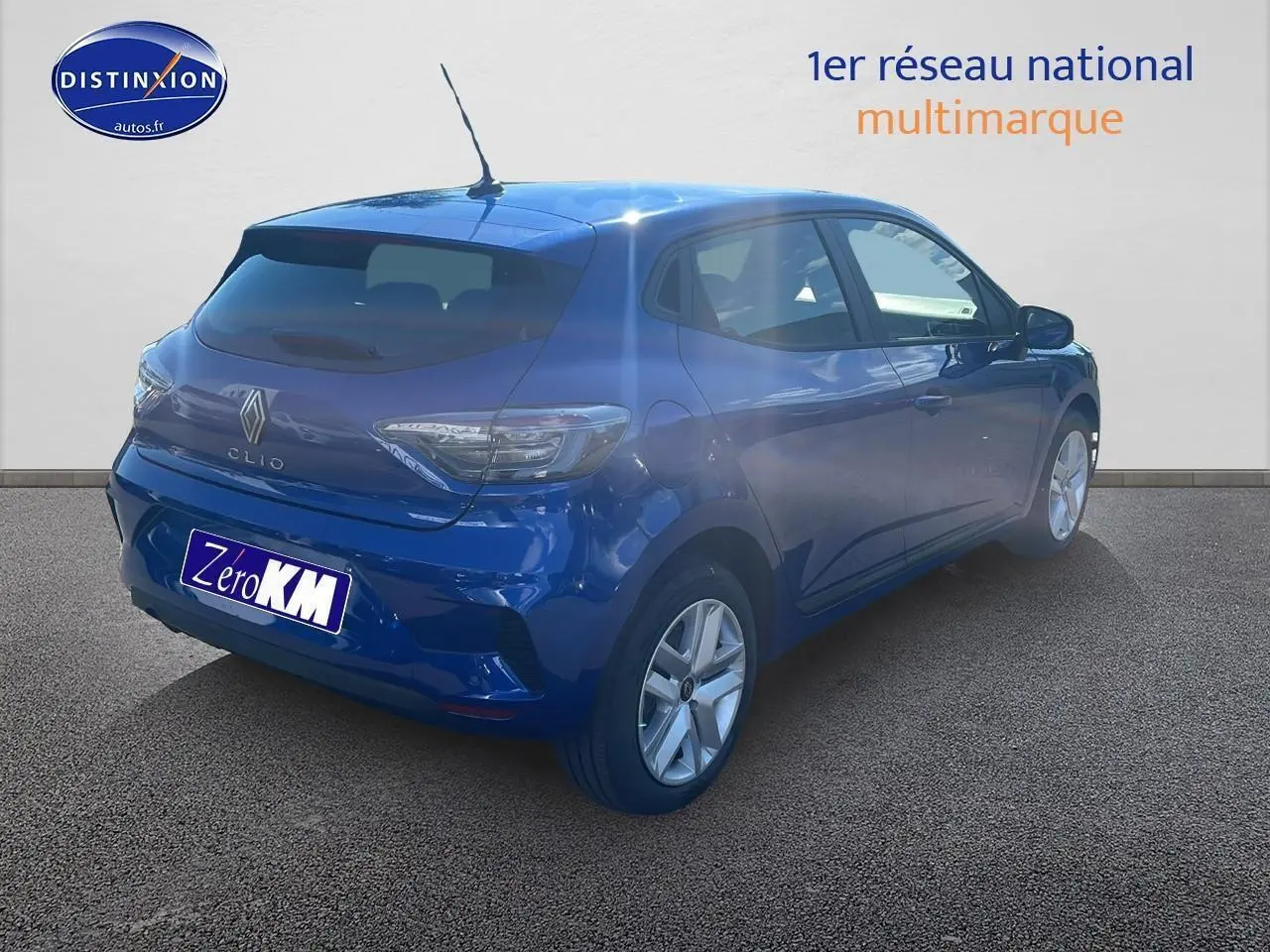 Renault Clio V bleu iron vue 3/4 arrière droit, avec feux arrière LED et becquet sur un sol goudronné.