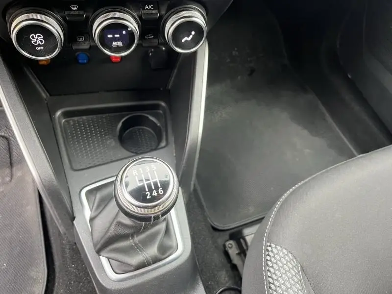 Gros plan sur la console centrale noire du Dacia Duster blanc avec levier de vitesses manuel et commandes de climatisation.
