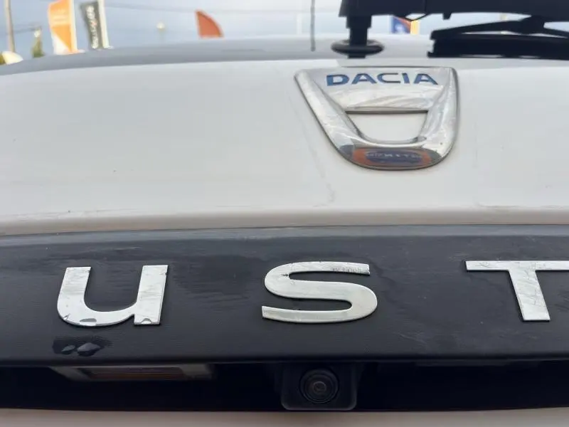 Gros plan sur le logo Dacia et le lettrage Duster en chrome sur le hayon arrière blanc glacier du SUV