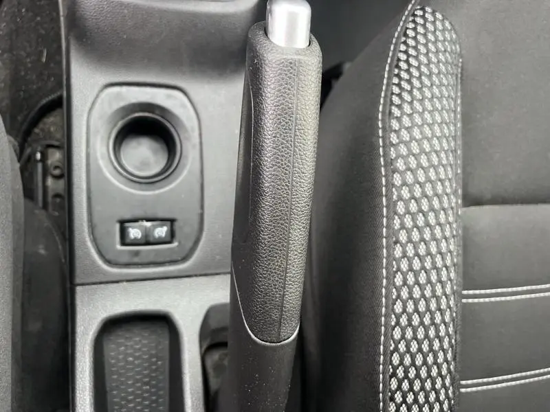 Gros plan sur le frein à main noir et la console centrale avec commandes et siège tissu noir à motifs du Dacia Duster Blanc Glacier 2019.