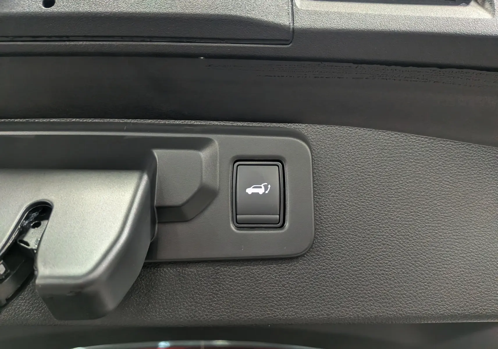 Bouton d'ouverture électrique du coffre sur le panneau intérieur noir d'une Renault SYMBIOZ Gris Cassiopé.