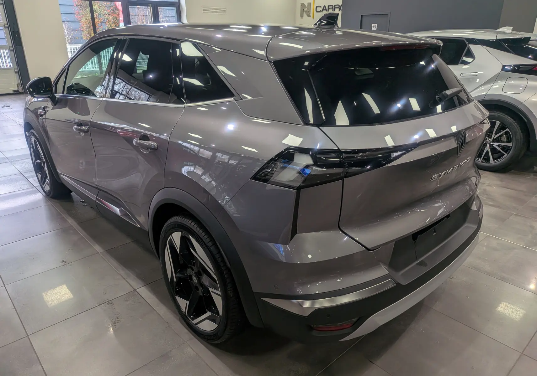 Vue 3/4 arrière droite du Renault SYMBIOZ gris Cassiopé avec feux arrière noirs et jantes bi-ton en showroom.