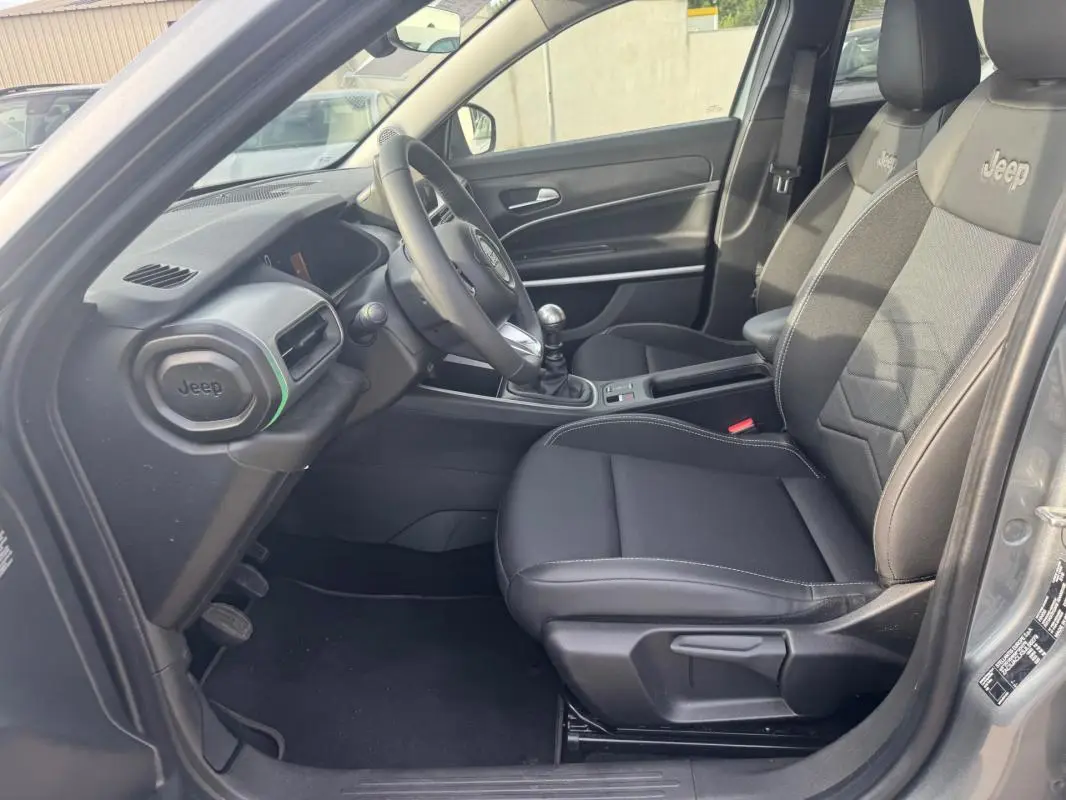 Vue intérieure côté conducteur du Jeep Avenger gris 2025, avec sièges noirs marqués Jeep et boîte manuelle visible.