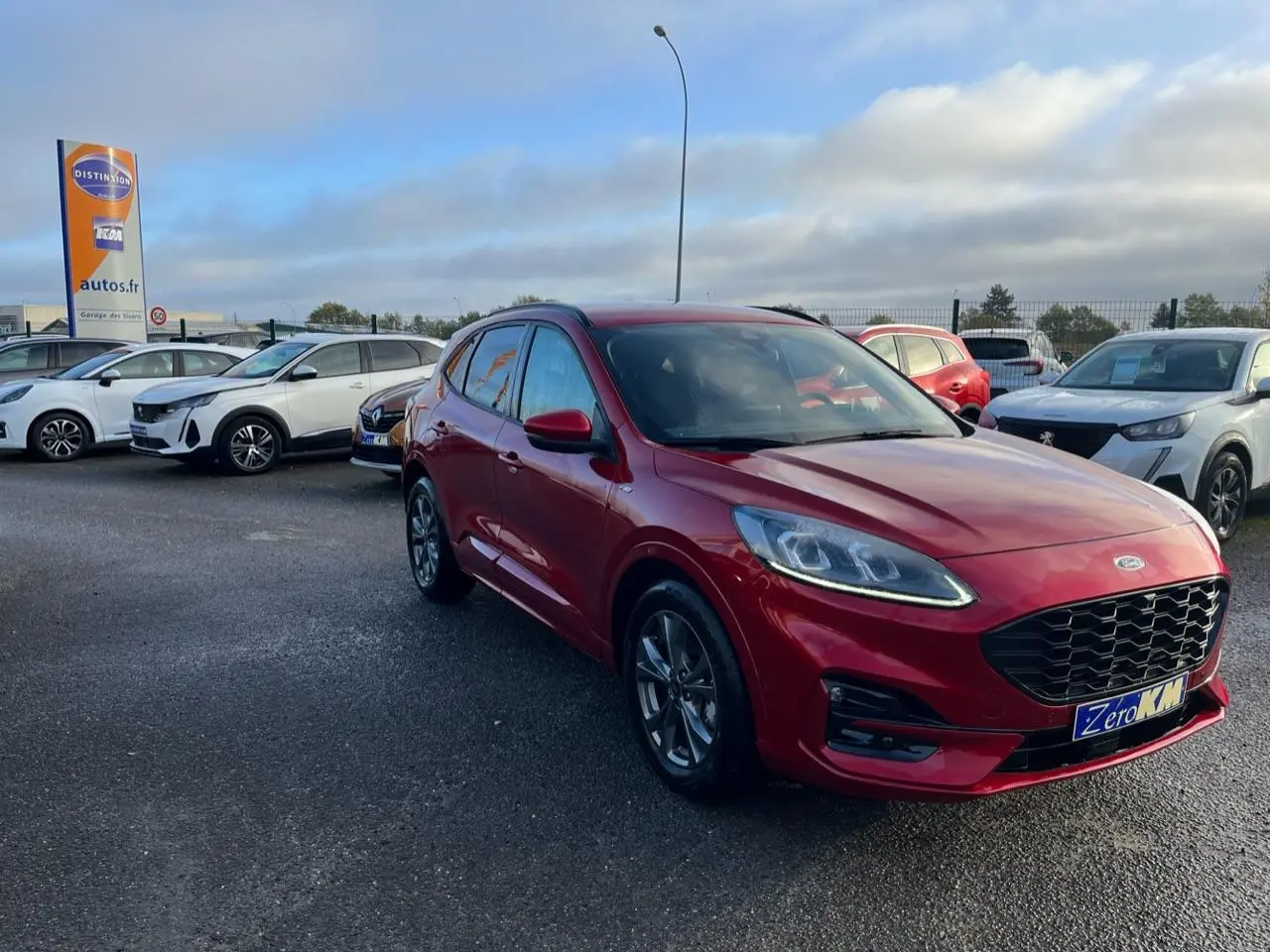Ford Kuga rouge Lucifer en 3/4 avant droit, avec calandre et jantes alliage ST-Line visibles sur parking.