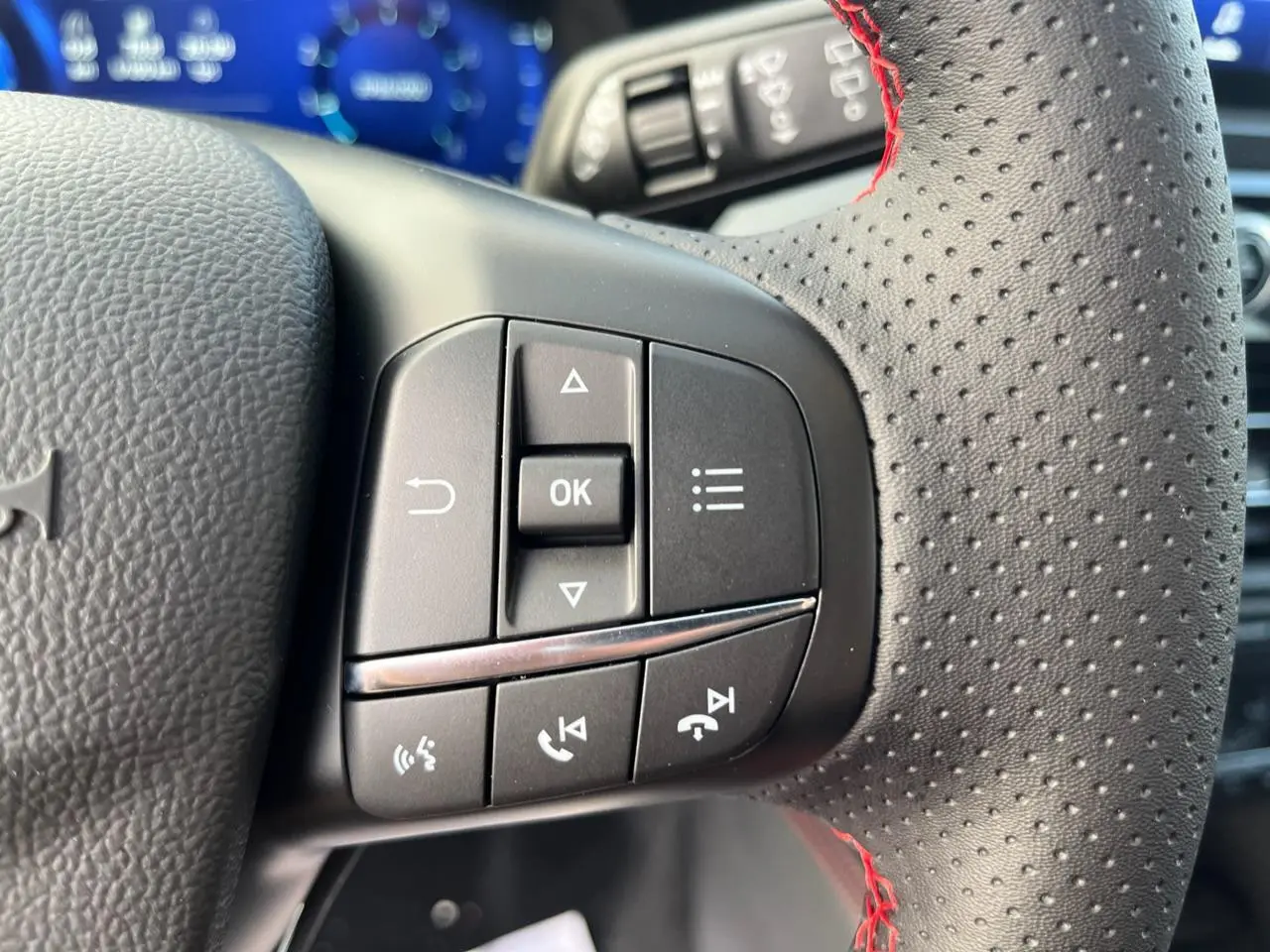Gros plan sur les commandes au volant à gauche du Ford Kuga ST-Line 2022, cuir perforé avec surpiqûres rouges.