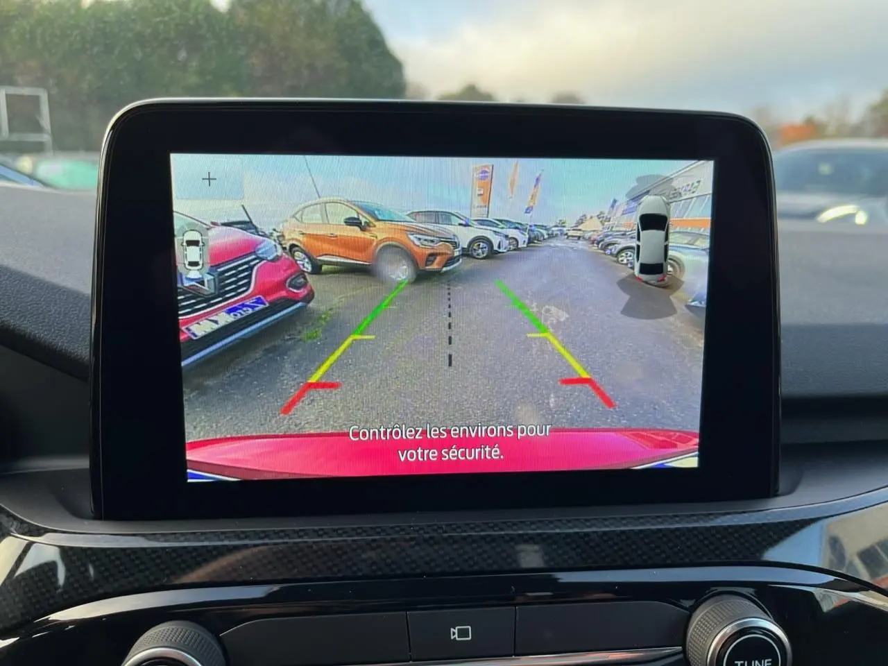 Vue écran intérieur montrant la caméra arrière du Ford Kuga rouge Lucifer en stationnement avec lignes d’aide au recul colorées.