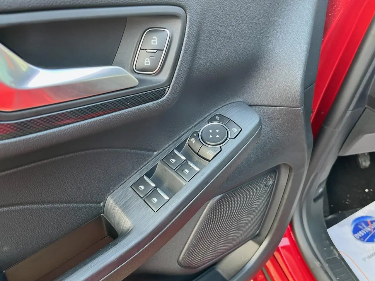 Détail de la porte côté conducteur du Ford Kuga rouge Lucifer 2022, montrant les commandes des vitres et la poignée intérieure.