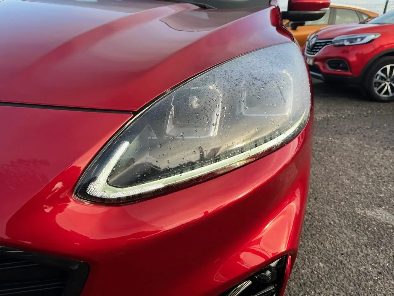 Gros plan sur le phare avant droit du Ford Kuga 1.5 EcoBoost rouge Lucifer avec peinture métallisée.