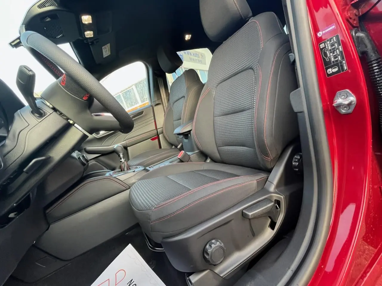 Vue intérieure côté conducteur du Ford Kuga rouge Lucifer 2022, sièges tissu noir avec surpiqûres rouges.