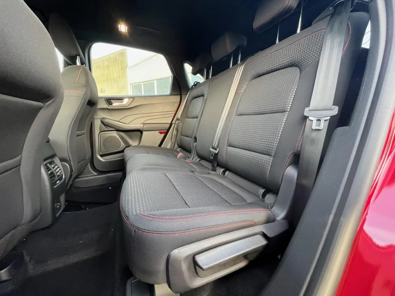 Vue intérieure côté droit sur la banquette arrière noire avec surpiqûres rouges du Ford Kuga 1.5 EcoBoost rouge Lucifer 2022.