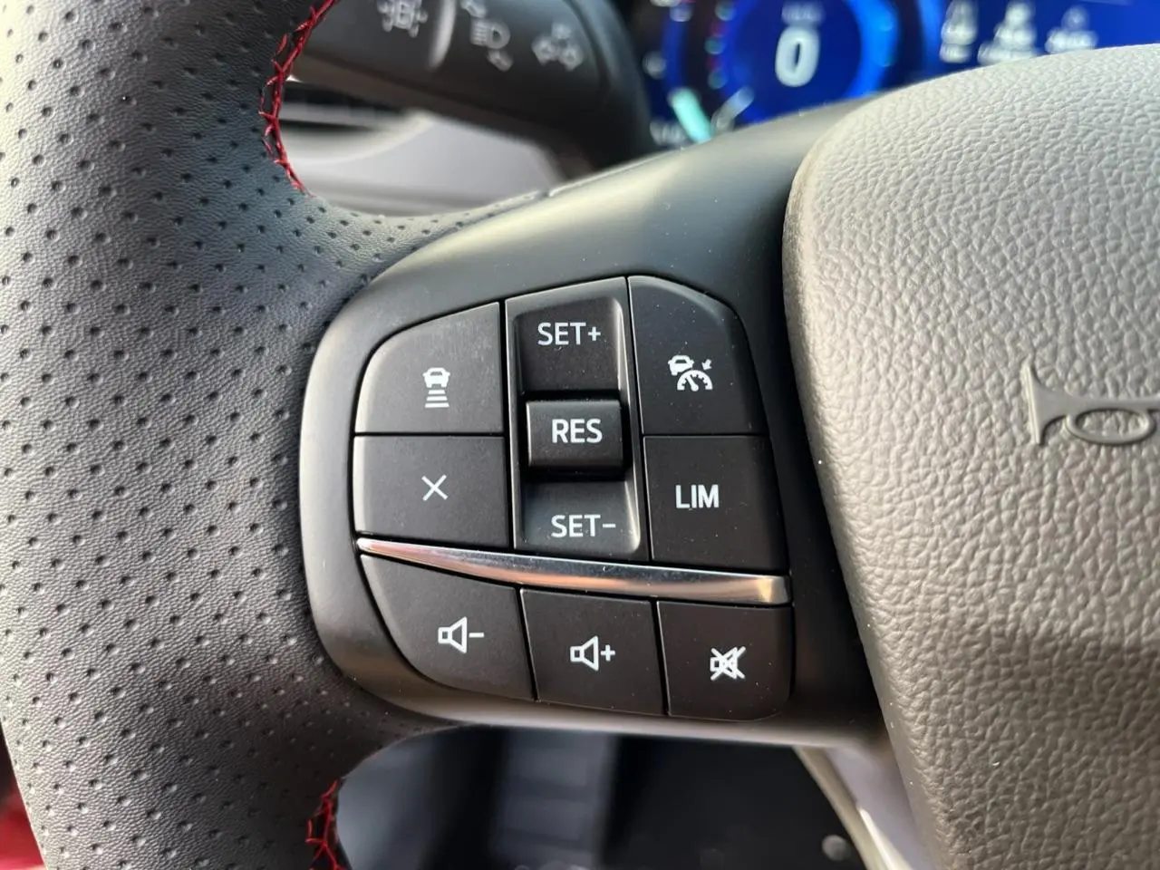 Gros plan sur les commandes au volant côté gauche du Ford Kuga rouge Lucifer, avec surpiqûres rouges visibles.