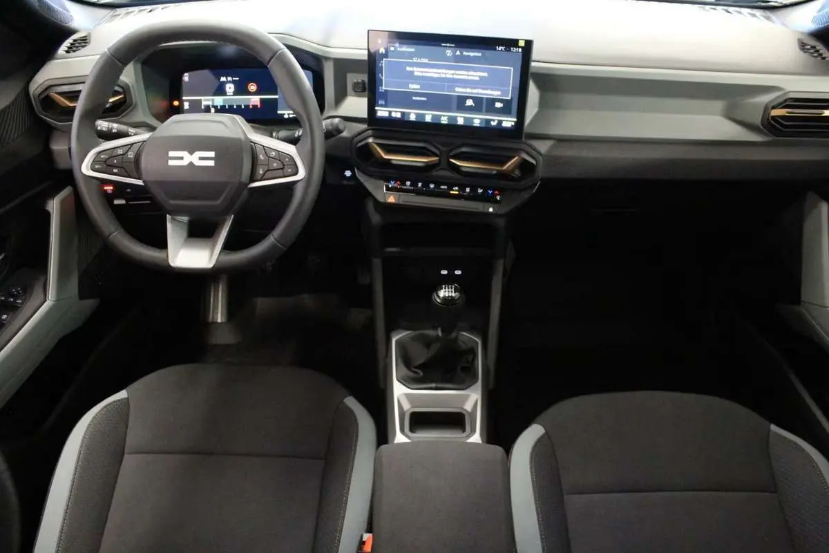 Vue intérieure avant du tableau de bord et volant cuir noir du Dacia Bigster gris schiste avec écran tactile central et boîte manuelle.