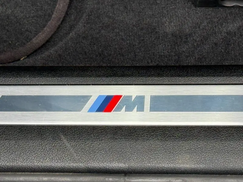 Gros plan sur la plaque de seuil de porte avec logo BMW M sur fond noir et métal brossé.