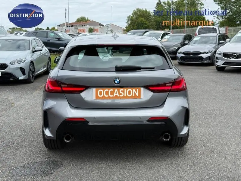 Vue arrière d'une BMW Série 1 118dA M Sport gris métallisé avec double sortie d'échappement et feux LED allumés.