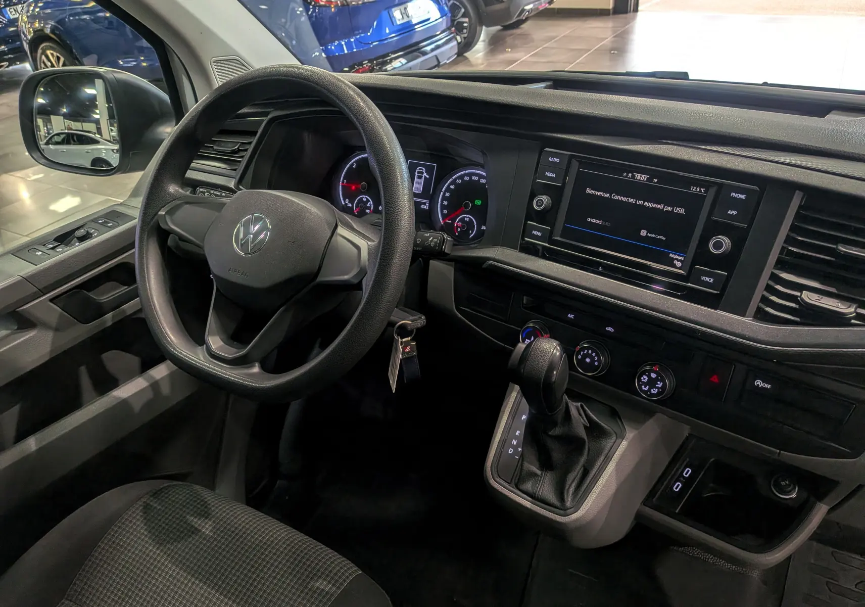 Vue intérieure côté conducteur du Volkswagen Transporter 6.1 blanc, avec tableau de bord numérique et boîte automatique.
