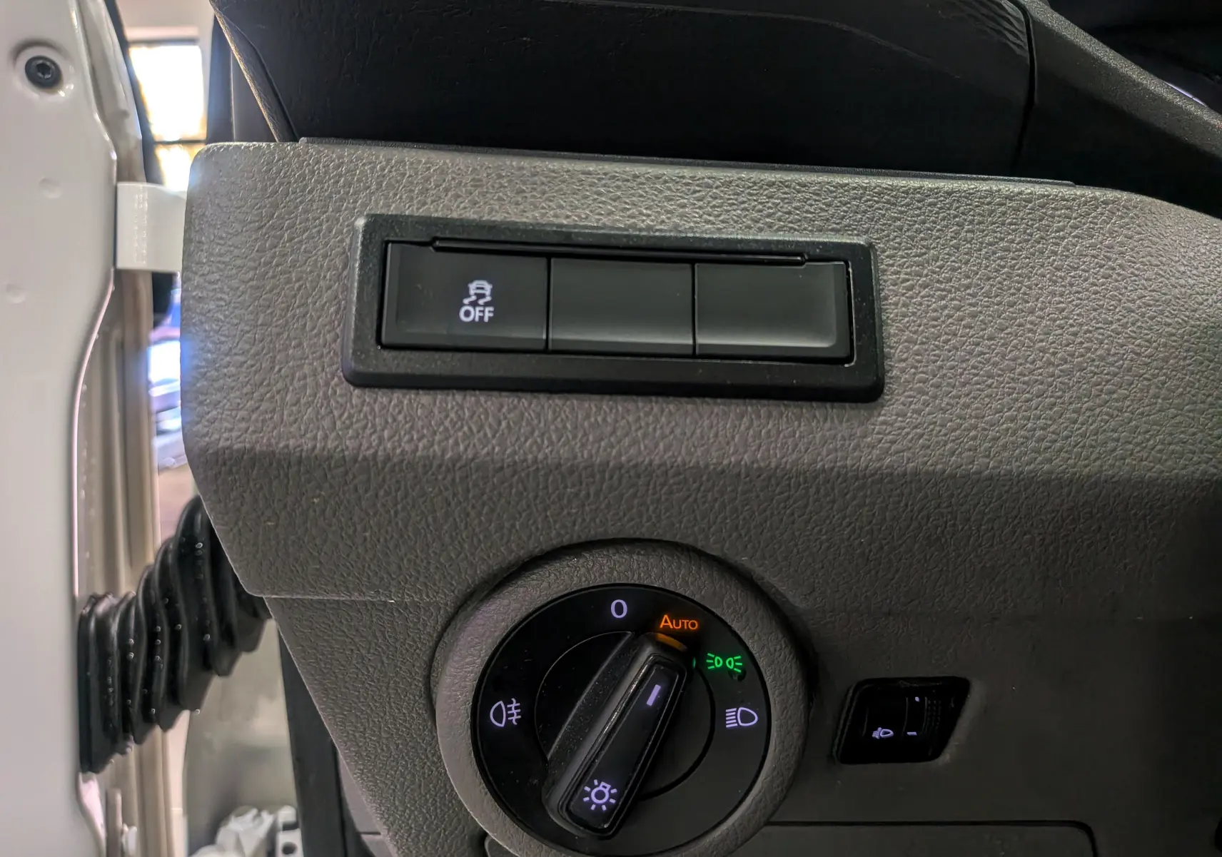 Gros plan sur le tableau de bord côté gauche du Volkswagen Transporter 6.1 blanc, montrant la commande des phares et le bouton de stabilité.