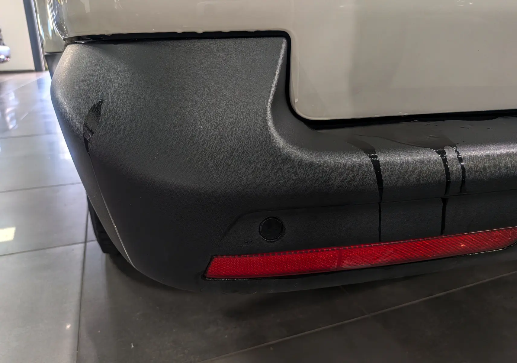 Gros plan sur le coin arrière droit du pare-chocs noir avec feu réfléchissant rouge du Volkswagen Transporter 6.1 blanc Candy.