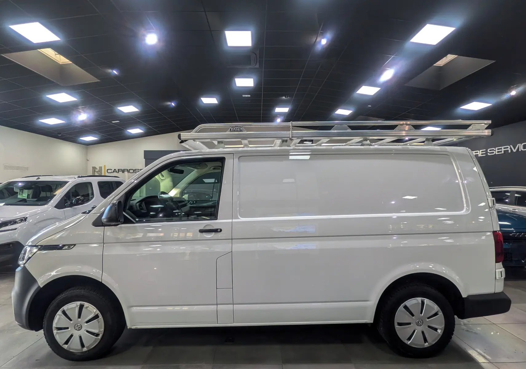 Vue de profil côté gauche d'un Volkswagen Transporter 6.1 Van blanc Candy avec galerie de toit en intérieur showroom.