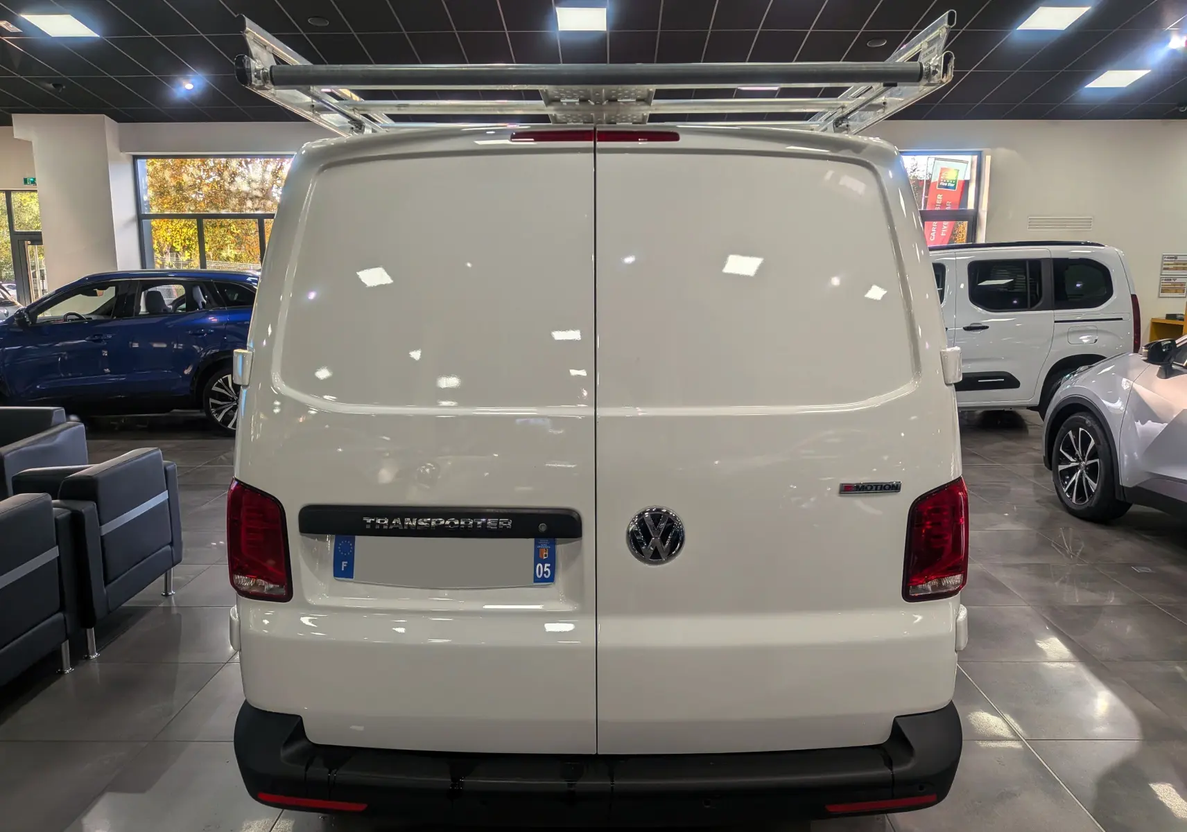 Vue arrière d'un Volkswagen Transporter 6.1 blanc Candy avec galerie de toit et badge 4MOTION visible en intérieur showroom.