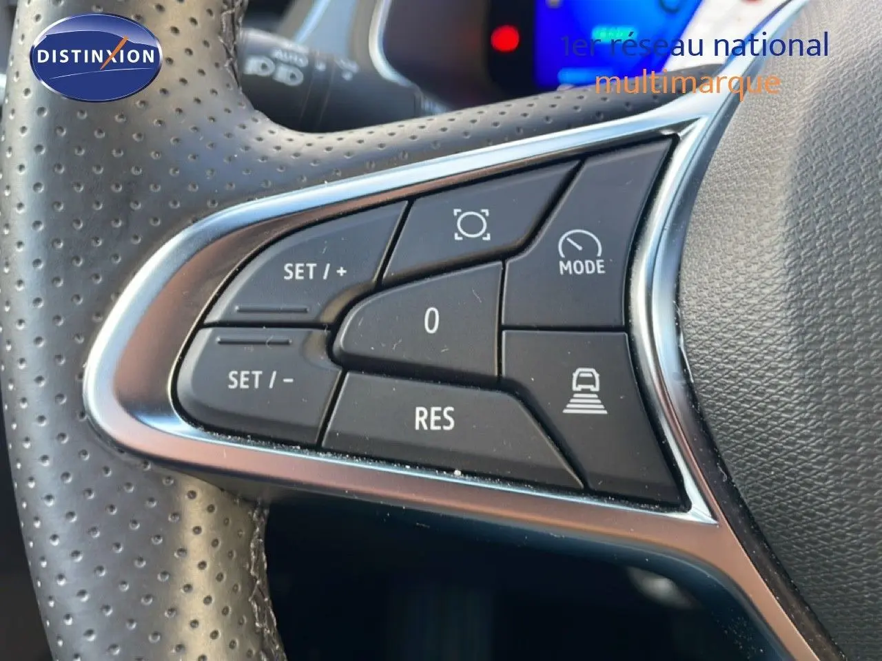 Gros plan sur les commandes au volant en cuir perforé du Renault Symbioz gris Cassiopée, mettant en avant les boutons de régulateur et mode conduite.