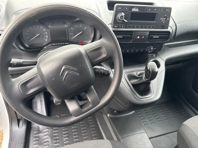 Vue intérieure du poste de conduite du Citroën Berlingo Fourgon blanc, volant, tableau de bord et levier de vitesses manuelle visibles.