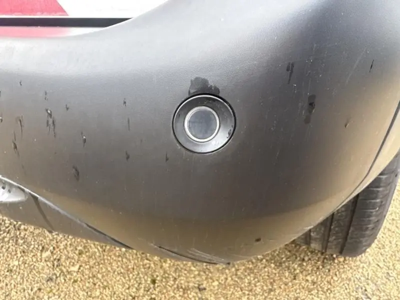 Gros plan sur un capteur de stationnement arrière intégré dans le pare-chocs noir d'un Citroën Berlingo blanc.
