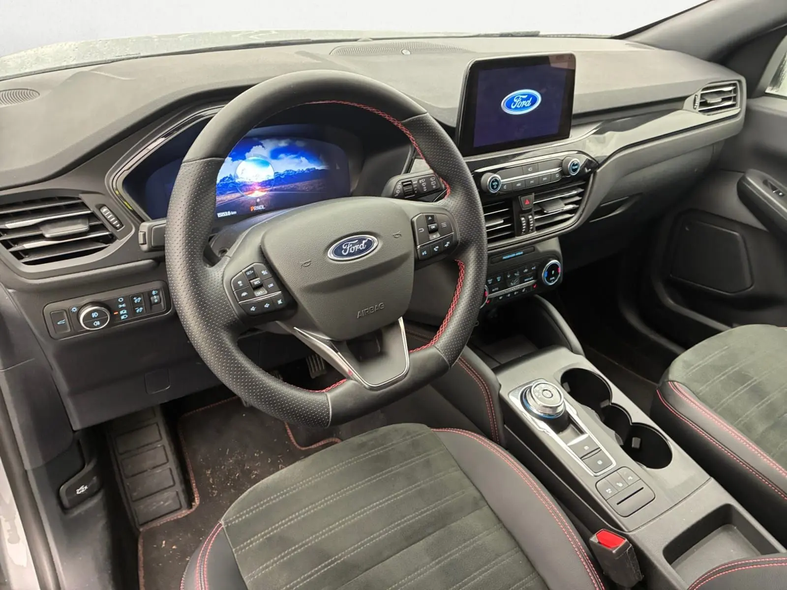 Vue intérieure côté conducteur du Ford Kuga 2024 gris, volant multifonctions, écran tactile et console centrale avec molette.