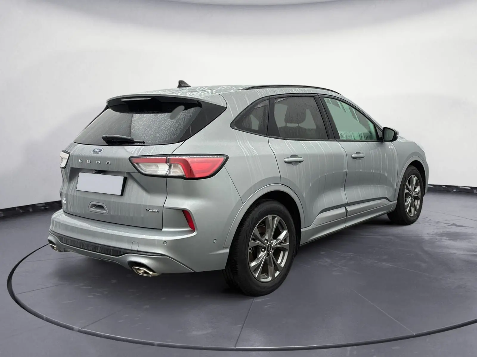 Vue 3/4 arrière droite d'un Ford Kuga gris 2024 hybride essence avec finition ST-Line X et double sortie d'échappement.