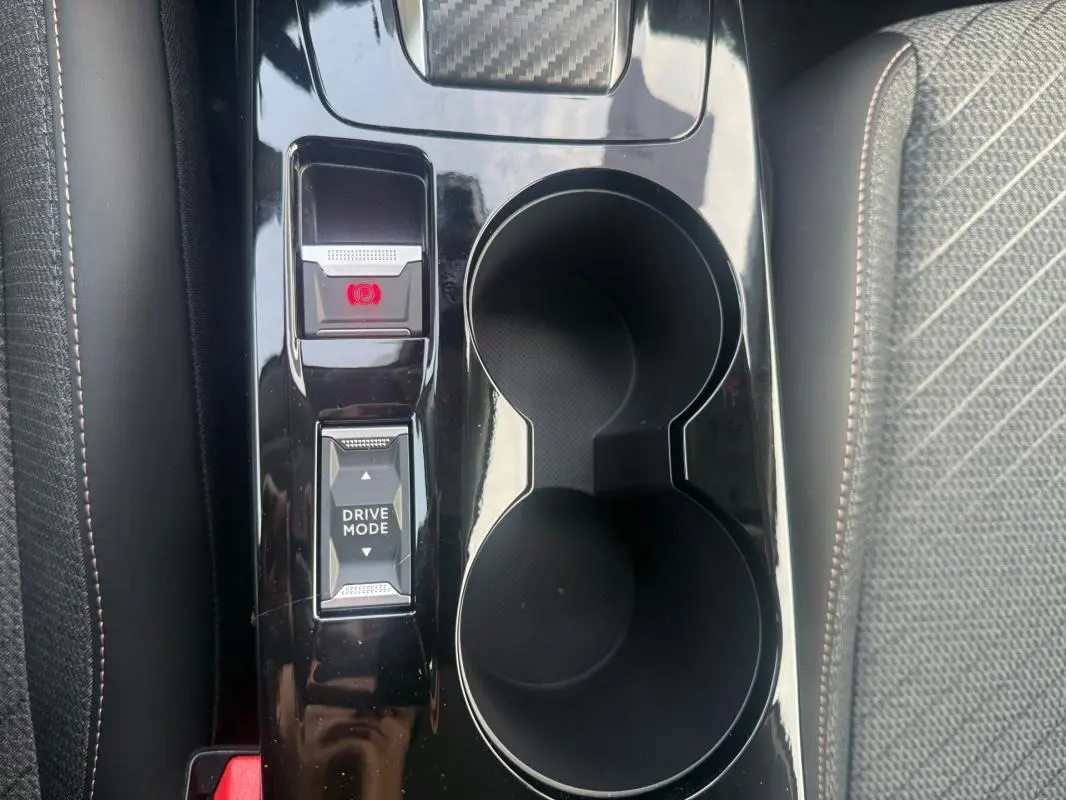 Gros plan sur la console centrale noire brillante de la Peugeot 208 gris, avec bouton frein à main électronique et mode de conduite.