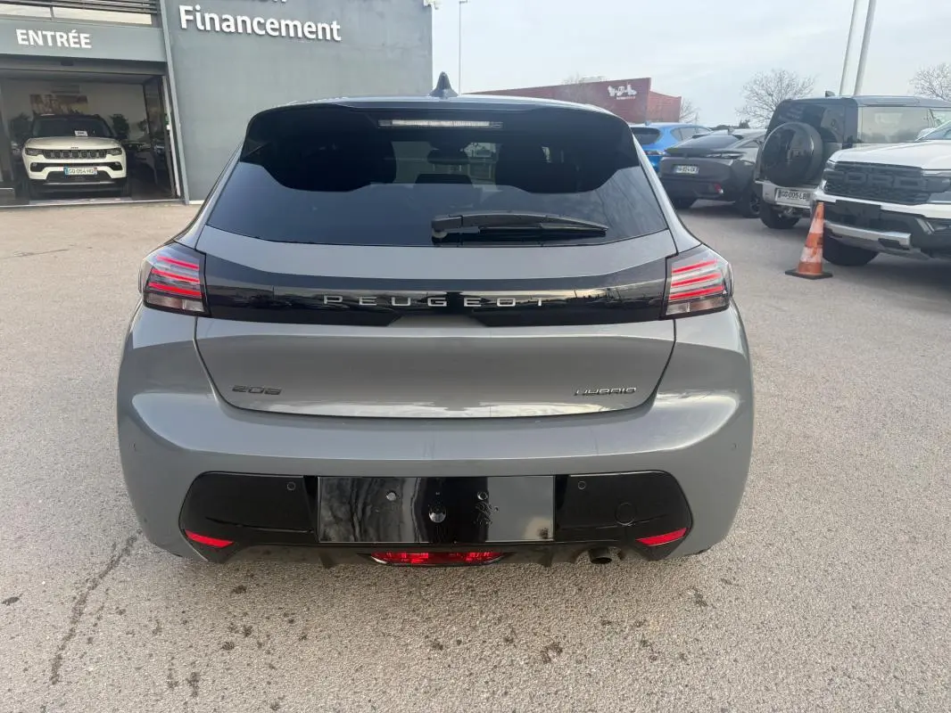Vue arrière d'une Peugeot 208 Hybrid gris 2025 avec feux LED et lunette arrière teintée, stationnée en extérieur.