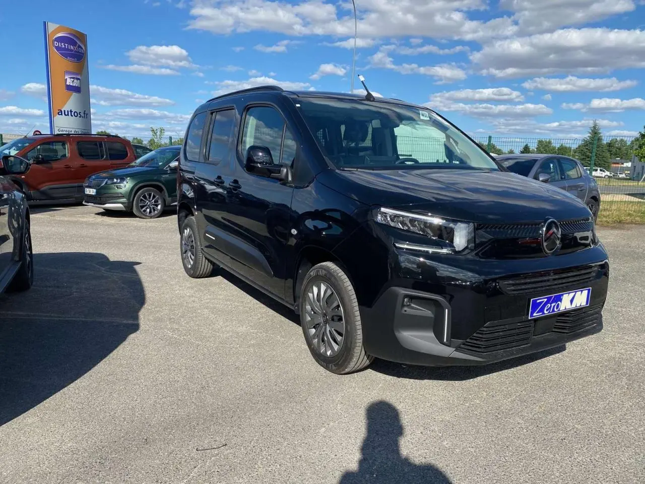 Vue 3/4 avant droit d'un Citroën Berlingo noir métallisé garé en extérieur sous un ciel bleu avec quelques nuages.