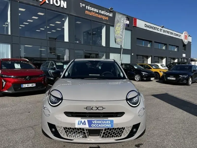 Vue avant d'une FIAT 600 T-Gen 3 beige 2025 avec phares ronds et calandre basse distinctive, devant un concessionnaire multimarque.