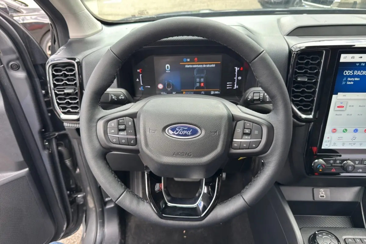 Vue intérieure centrée sur le volant cuir multifonctions du Ford Ranger gris carbone avec tableau de bord digital et écran tactile.