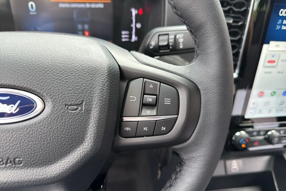 Gros plan sur le volant cuir du Ford Ranger gris carbone, avec commandes multifonctions et tableau de bord numérique en arrière-plan.
