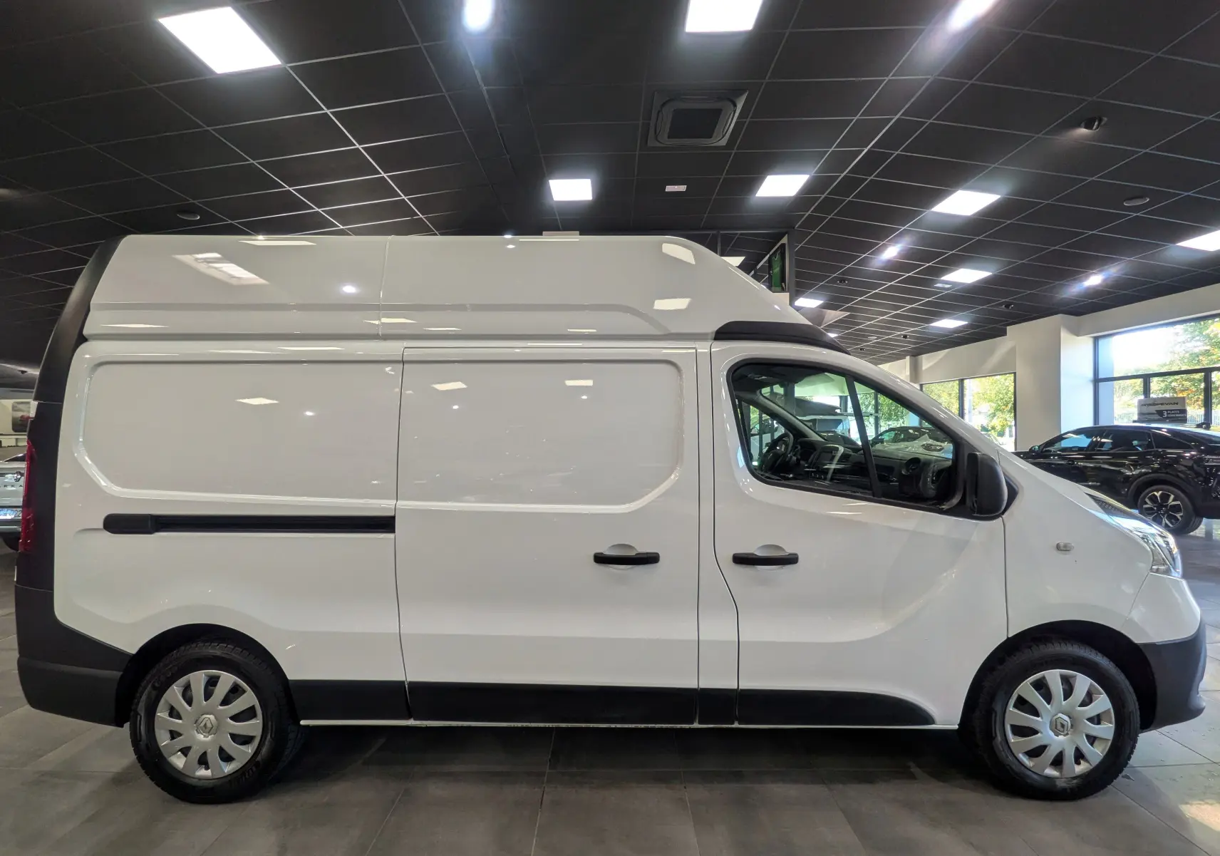 Profil droit du Renault Trafic Fourgon L2H2 blanc glacier, vue en intérieur avec toit surélevé et jantes acier.