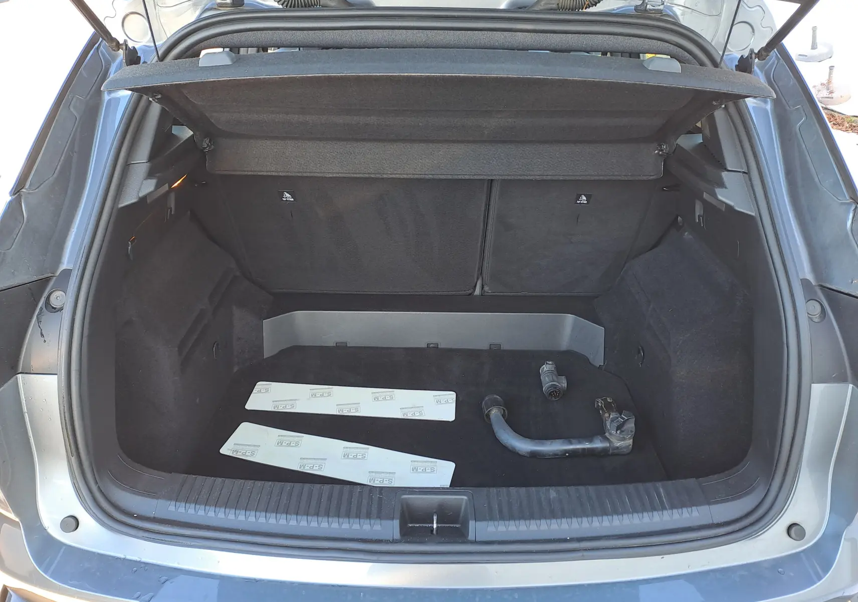 Coffre ouvert vu de l'arrière d'un Renault Austral gris schiste avec accessoires posés à l'intérieur.