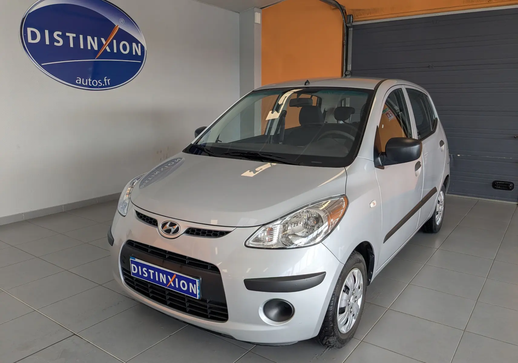Vue 3/4 avant droite d'une Hyundai i10 gris clair de 2010, compacte avec cinq portes et rétroviseurs noirs.