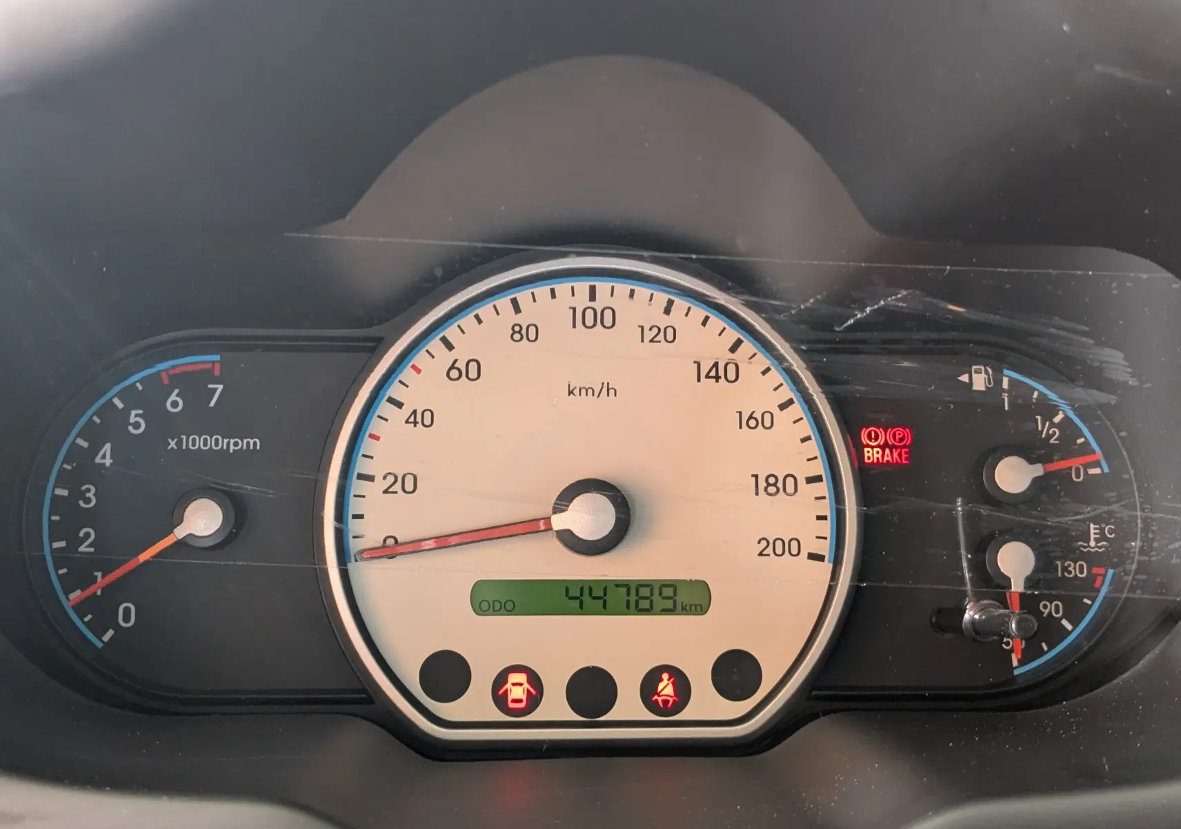 Vue rapprochée du tableau de bord gris clair d'une Hyundai i10 2010, affichant 44 789 km et voyants allumés.