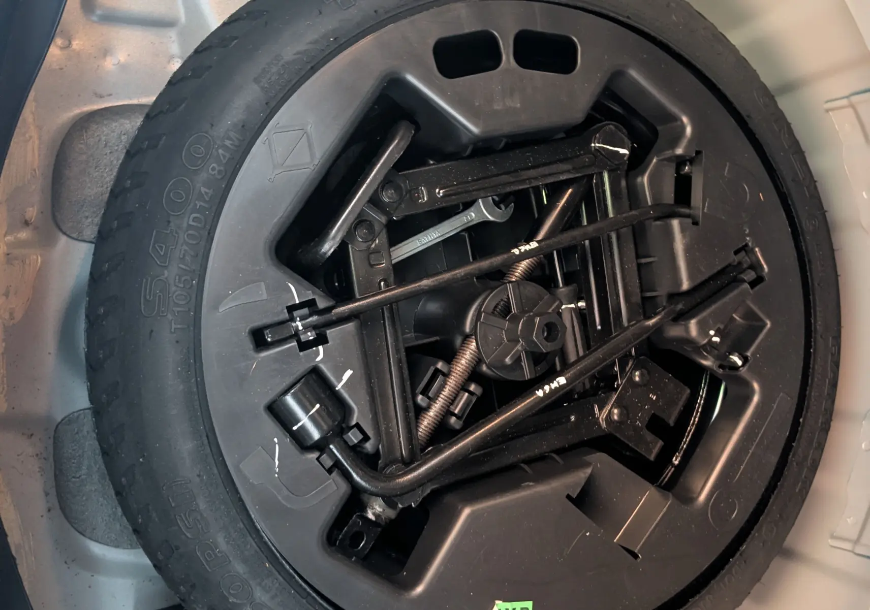 Gros plan sur la roue de secours noire et ses outils de bord dans le coffre gris clair d'une Hyundai i10 2010.