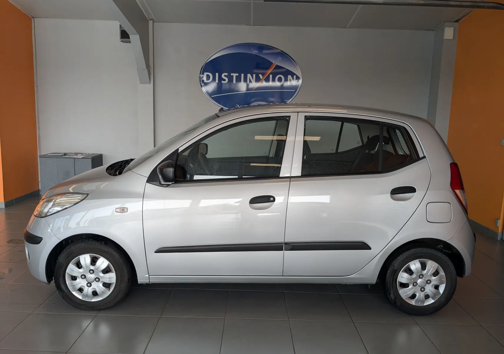 Vue de profil côté gauche d'une Hyundai i10 gris clair 2010, compacte avec cinq portes et jantes acier à enjoliveurs.