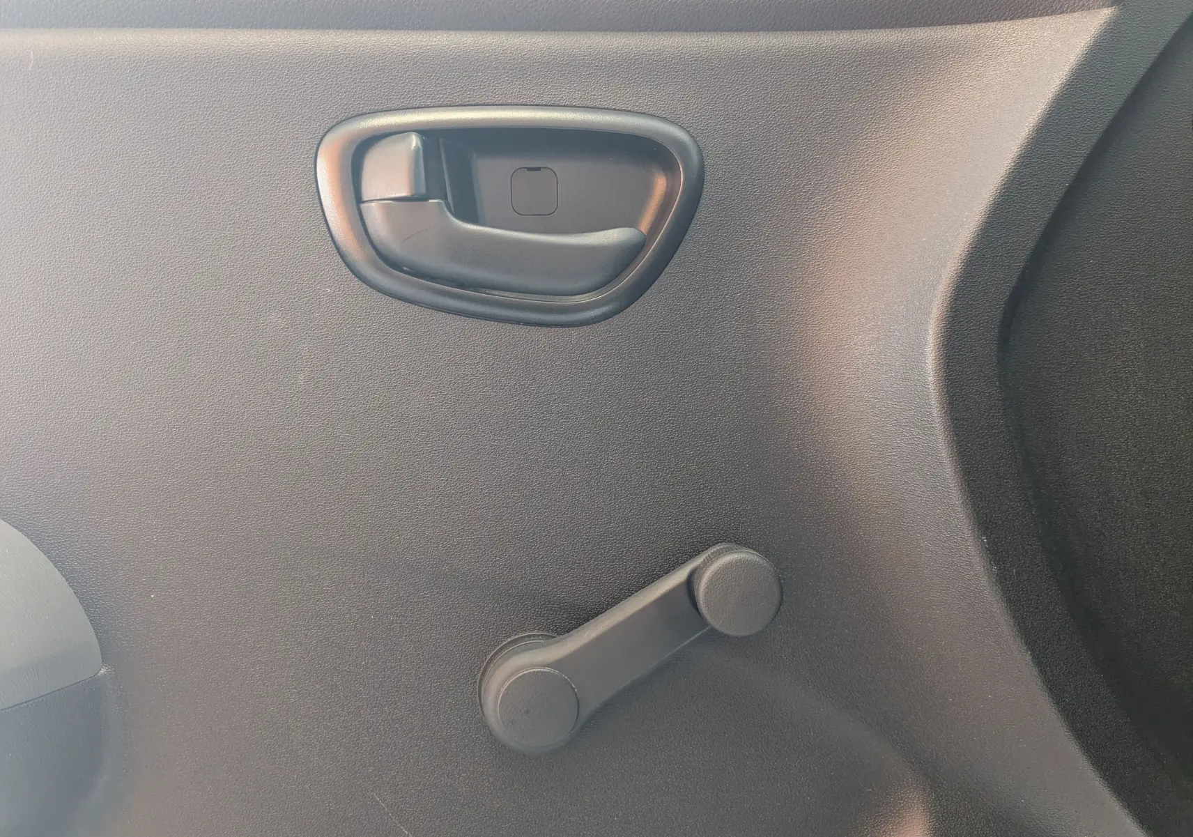 Poignée de porte intérieure noire et manivelle de vitre manuelle sur la porte côté droit d'une Hyundai i10 gris clair 2010.