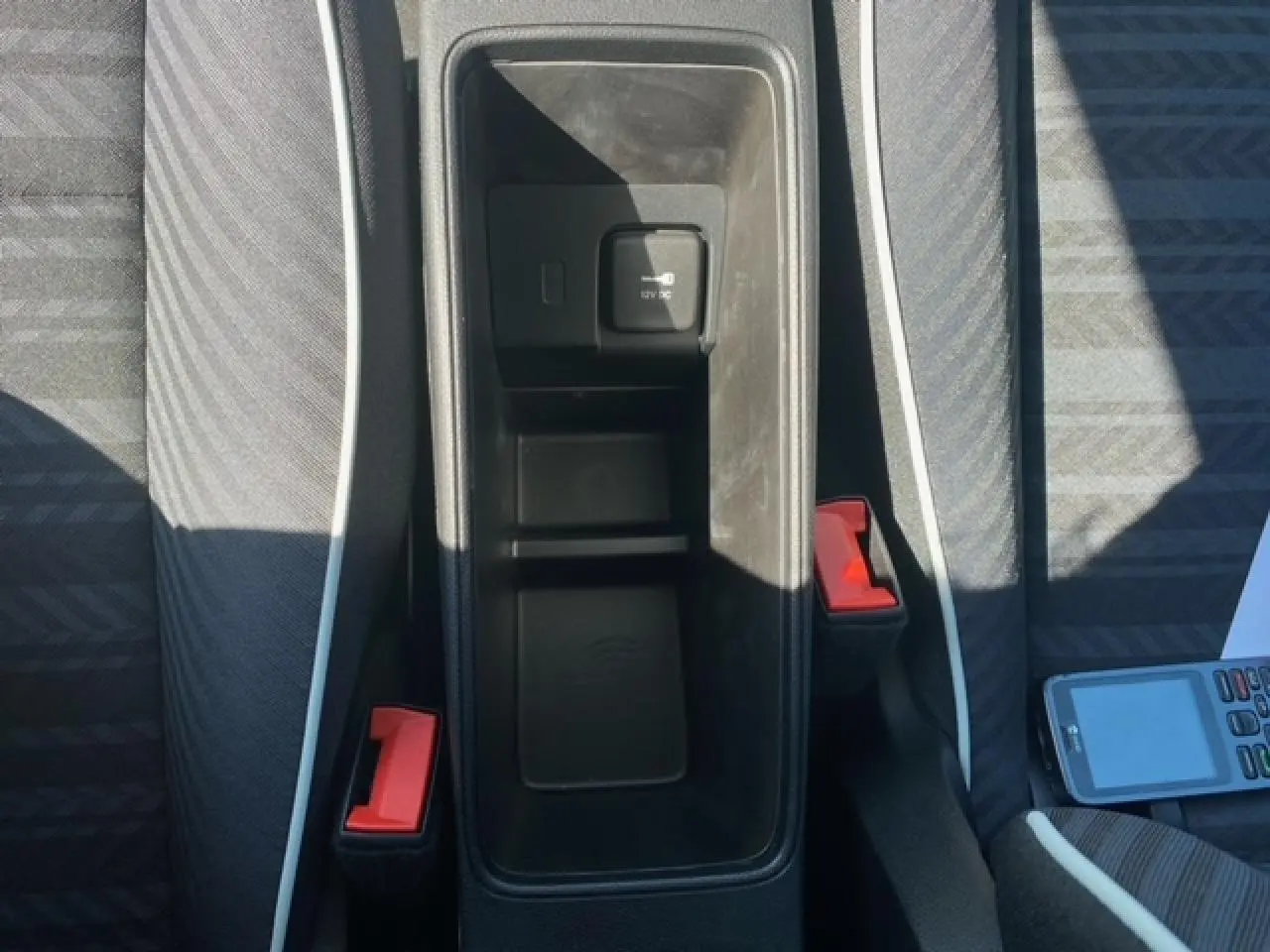 Vue plongeante sur le rangement central noir entre les sièges gris avec surpiqûres blanches de la Fiat 500 électrique blanche.