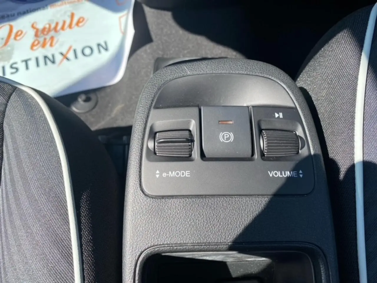 Gros plan sur la console centrale de la Fiat 500 électrique blanche, montrant les commandes e-mode, frein à main électrique et volume.