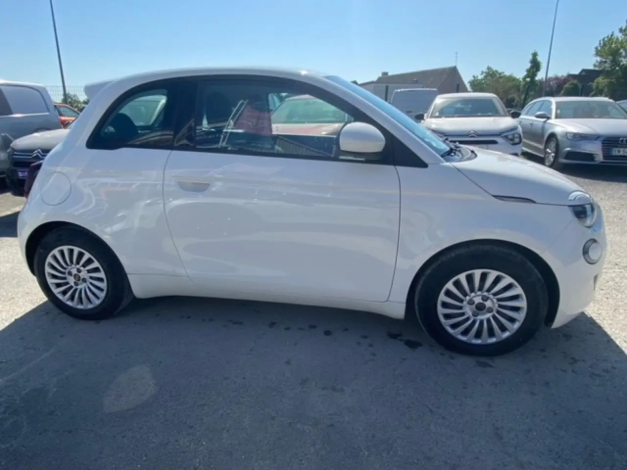 Vue de profil côté gauche d'une FIAT 500 électrique blanche métallisée, avec jantes originales et silhouette compacte.
