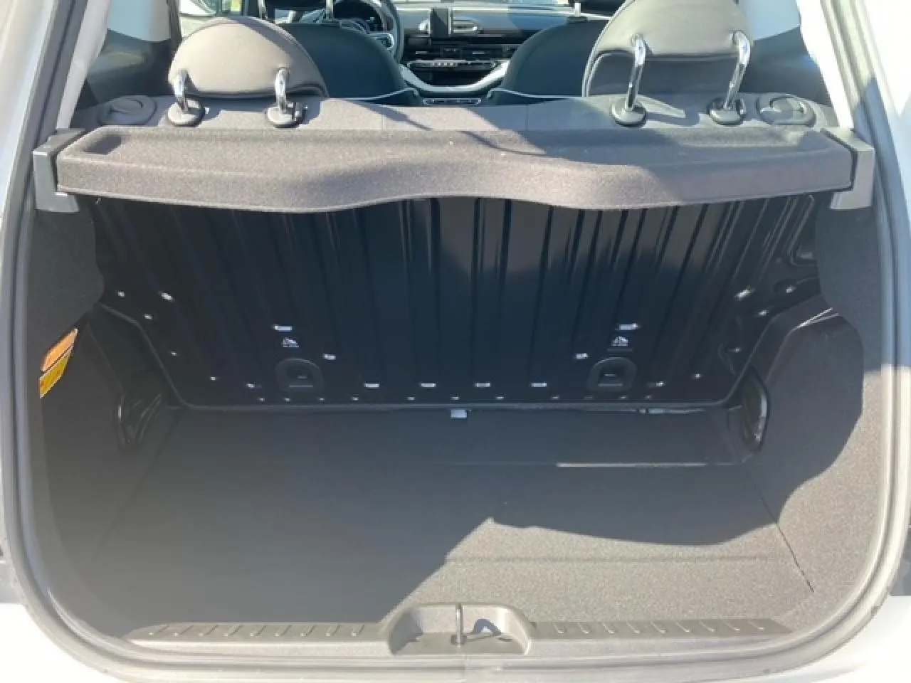 Vue du coffre ouvert d'une FIAT 500 électrique blanche, montrant l'espace de rangement et l'intérieur arrière du véhicule.